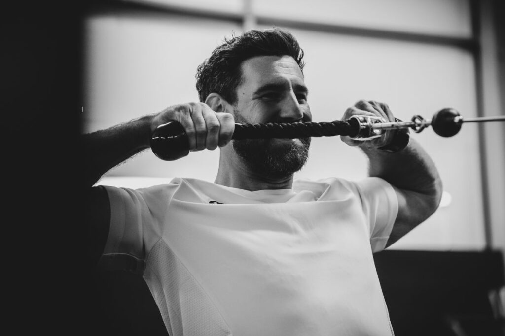 Man in the gym doing face pulls with cables.