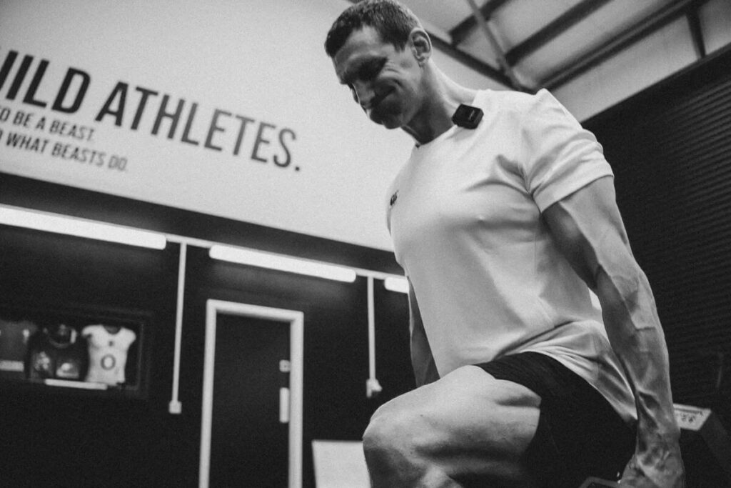 Sam Warburton doing a Bulgarian split squat at the gym with "Build Athletes" on the wall behind.