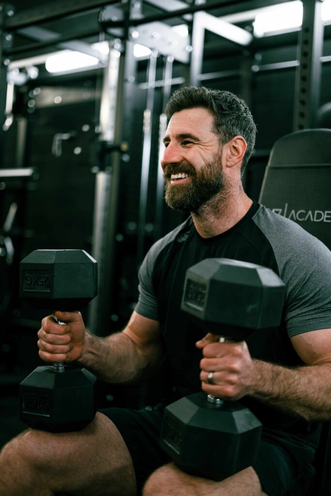 Josh sat down holding two dumbbells while smiling.