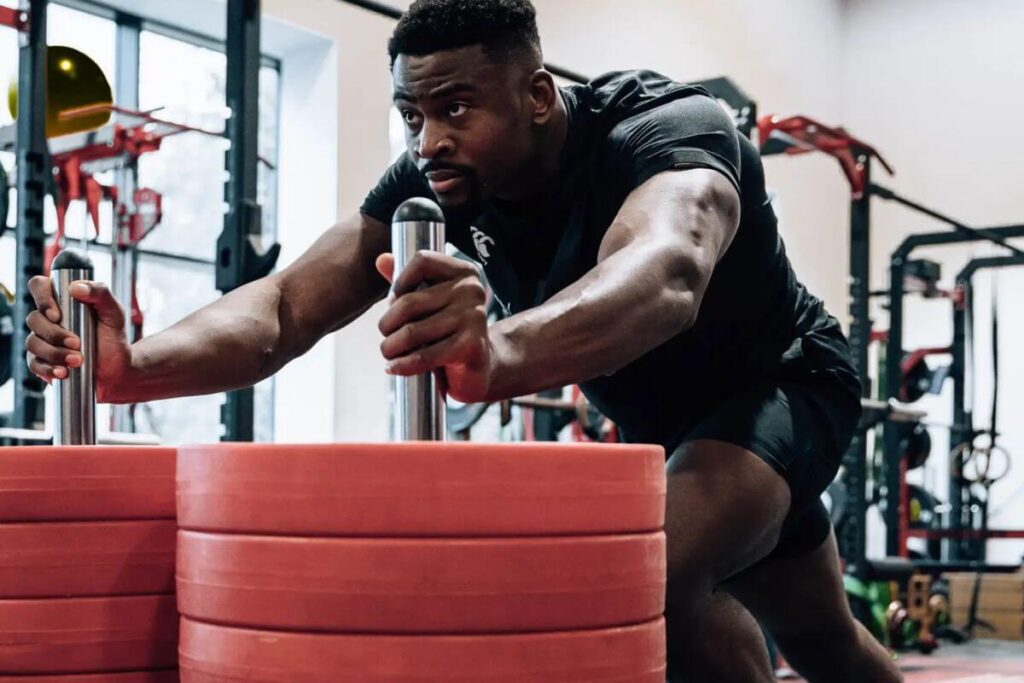 A man pushes a sled with red weights at the gym.